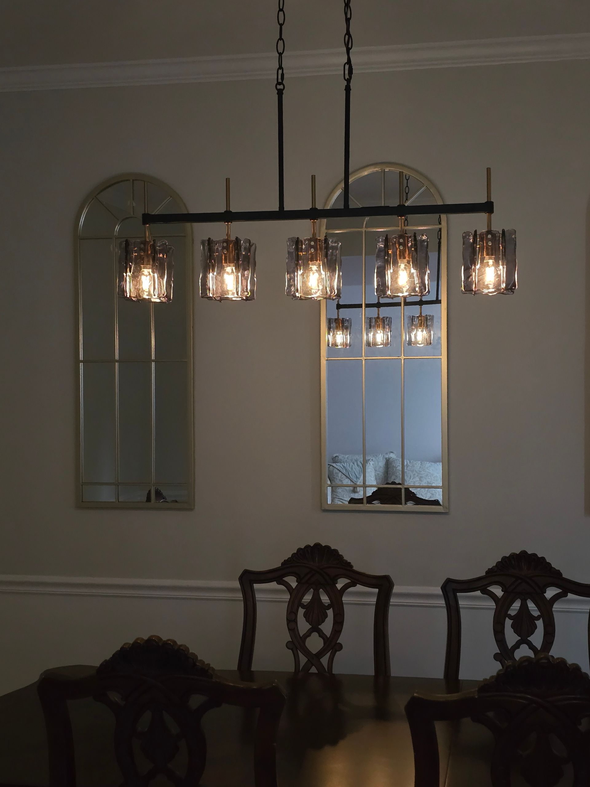 Hand adjusting a lit pendant light in a modern room with geometric wire shades