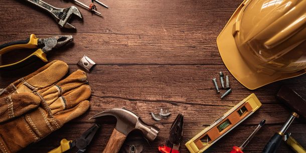 Construction tools and gloves on a wooden workbench with a yellow hard hat and level