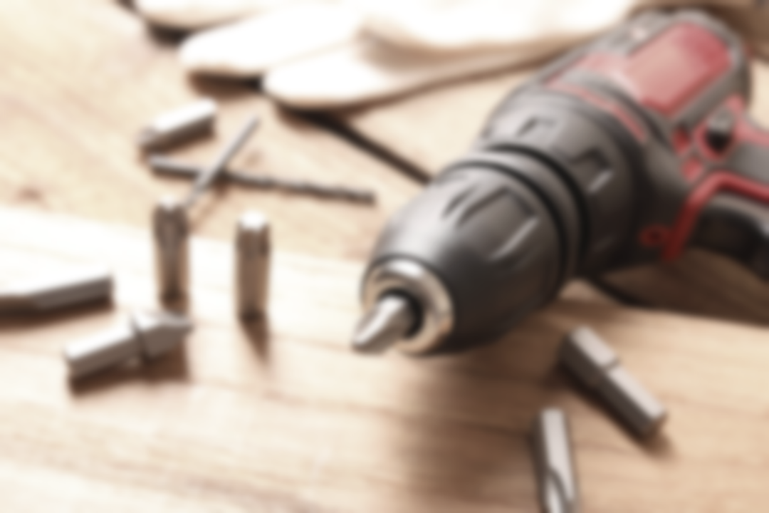Red cordless drill on a wooden workbench with scattered drill bits and screws