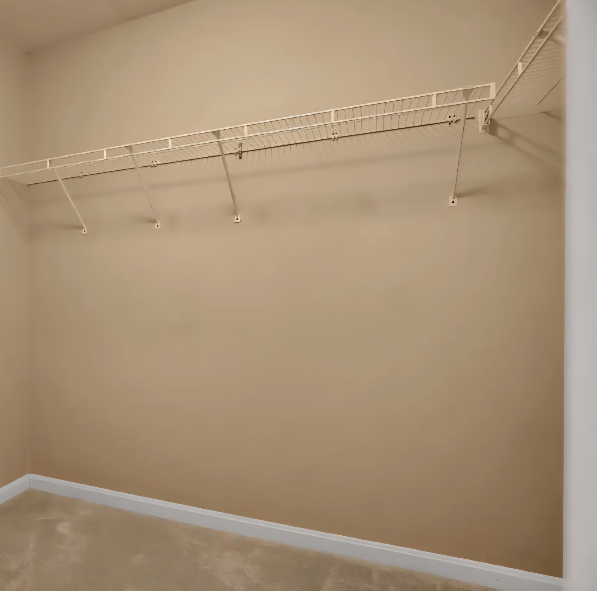 Empty beige closet with white wire shelving and carpeted floor
