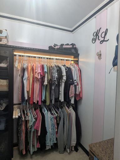Closet filled with hanging clothes in a small bedroom with white walls and black trim.