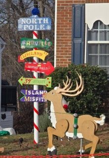 North Pole signpost with a decorative reindeer beside it and a brick building in the background