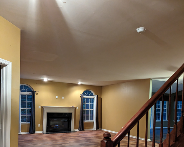Empty living room with beige walls, brown ceiling, fireplace, arched windows, and staircase railing.