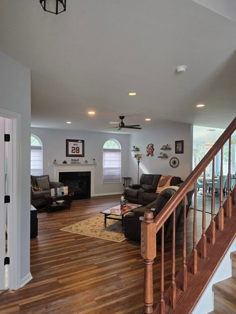 Living room with brown leather sofa, fireplace, wood staircase, and hardwood floors