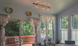 Bright living room with large windows, pink curtains, chandelier, and view of a wooden deck outside