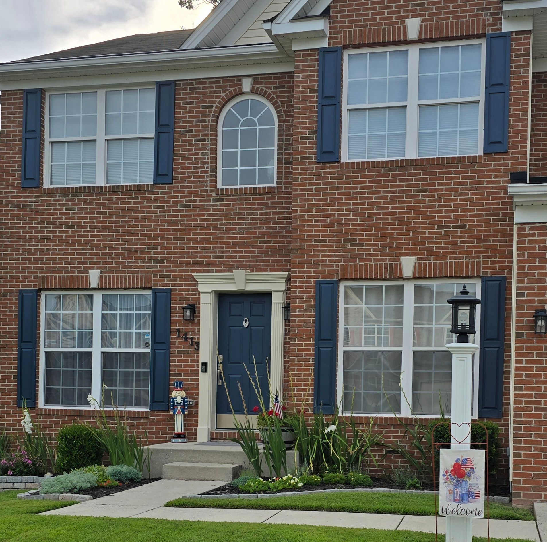 Two-story brick house with blue shutters, white-trimmed windows, and a dark blue front door