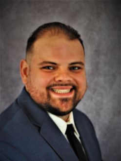 Smiling man in a navy suit and tie against a gray studio backdrop