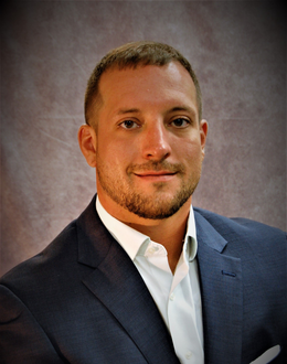 Professional headshot of a man in a navy suit and white shirt against a gray backdrop