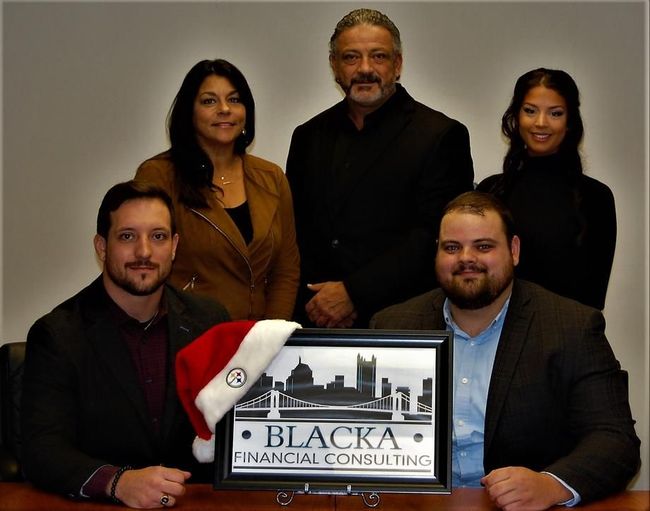 Five people posing behind a Blacka Financial Consulting sign, one wearing a Santa hat