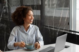 Person smiling at a laptop while holding a cup in a bright office.