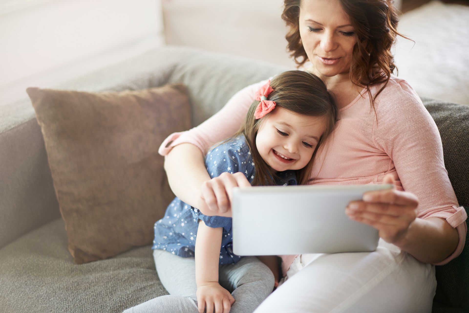 Family relaxing on a couch by a window, talking and laughing. Soft light fills the room.