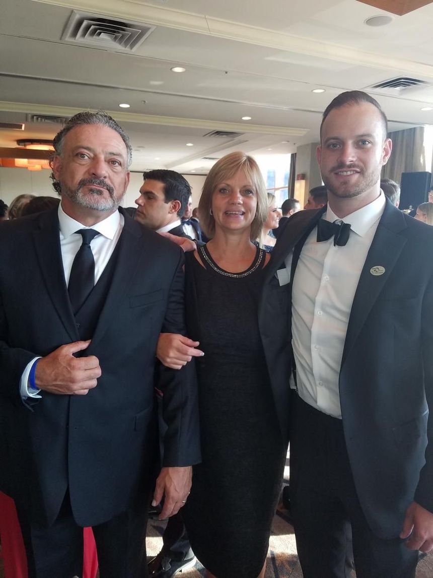 Three people in formal attire pose together indoors at a social event.