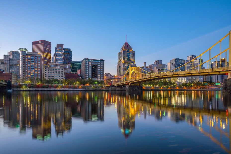 City skyline at dusk with bridge lights reflected on calm water.