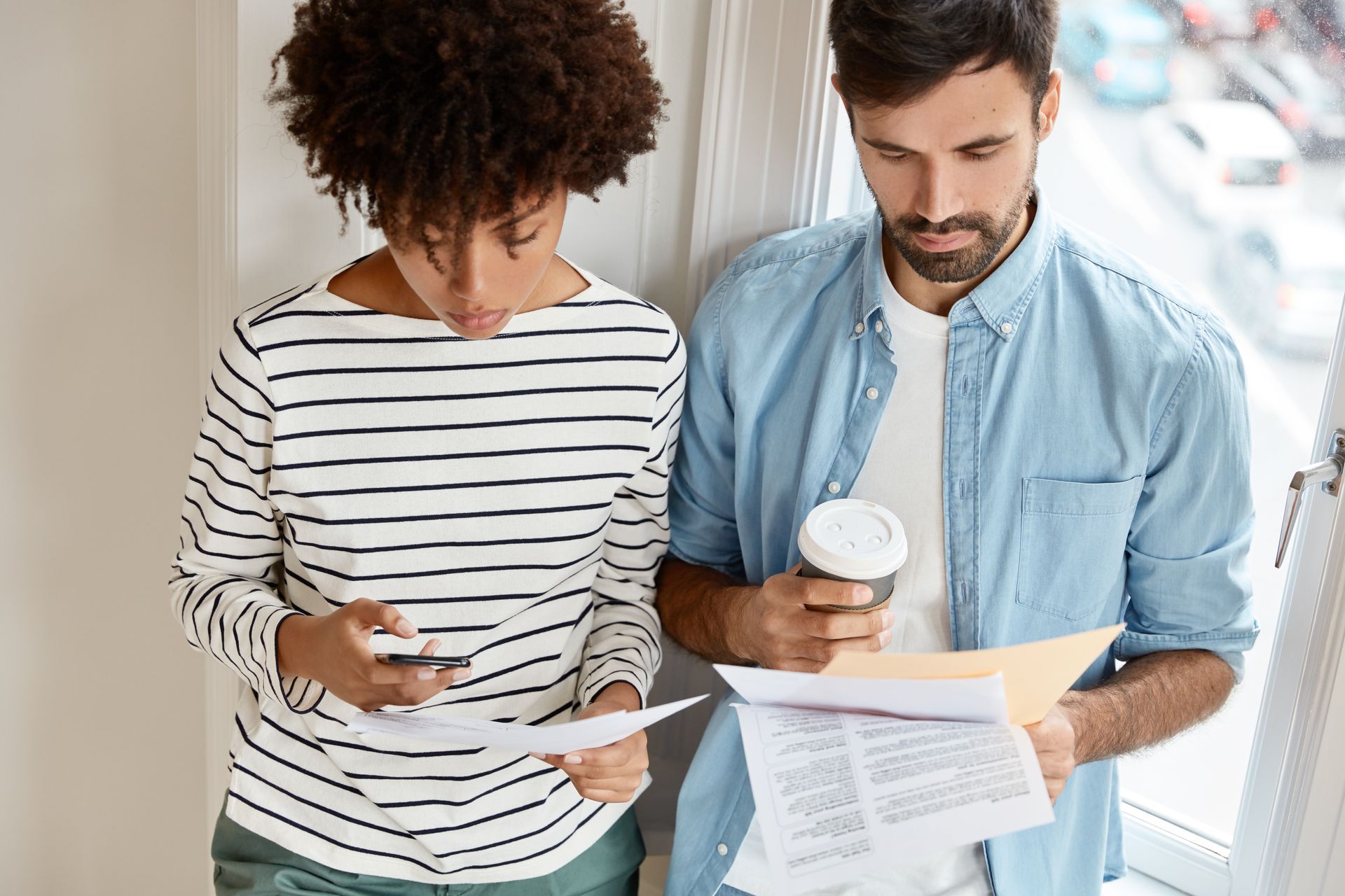 Two people reviewing papers together indoors, one holding a coffee cup.