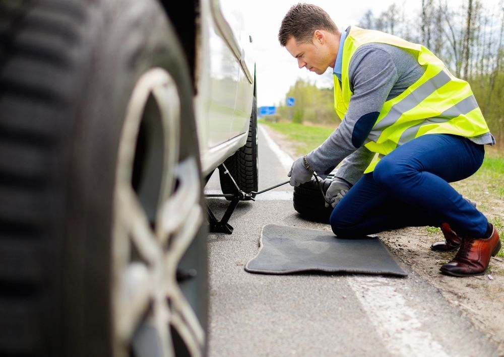 A Man is Changing a Tire on the Side of the Road — Cairns Roadside Assist In Innisfail, QLD