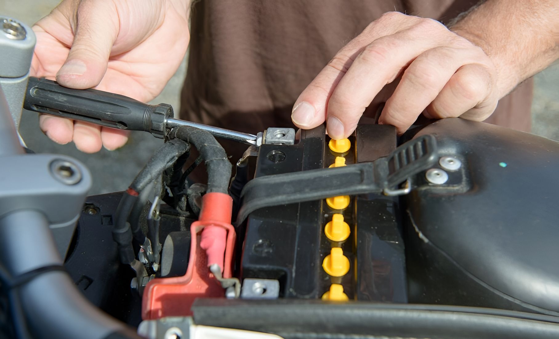 A Man Is Fixing A Motorcycle Battery With A Screwdriver — Cairns Roadside Assist In Mareeba, QLD