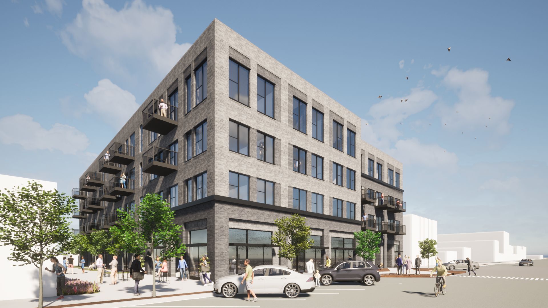 Multi-story brick building with balconies and ground-floor storefronts, street with cars and pedestrians.
