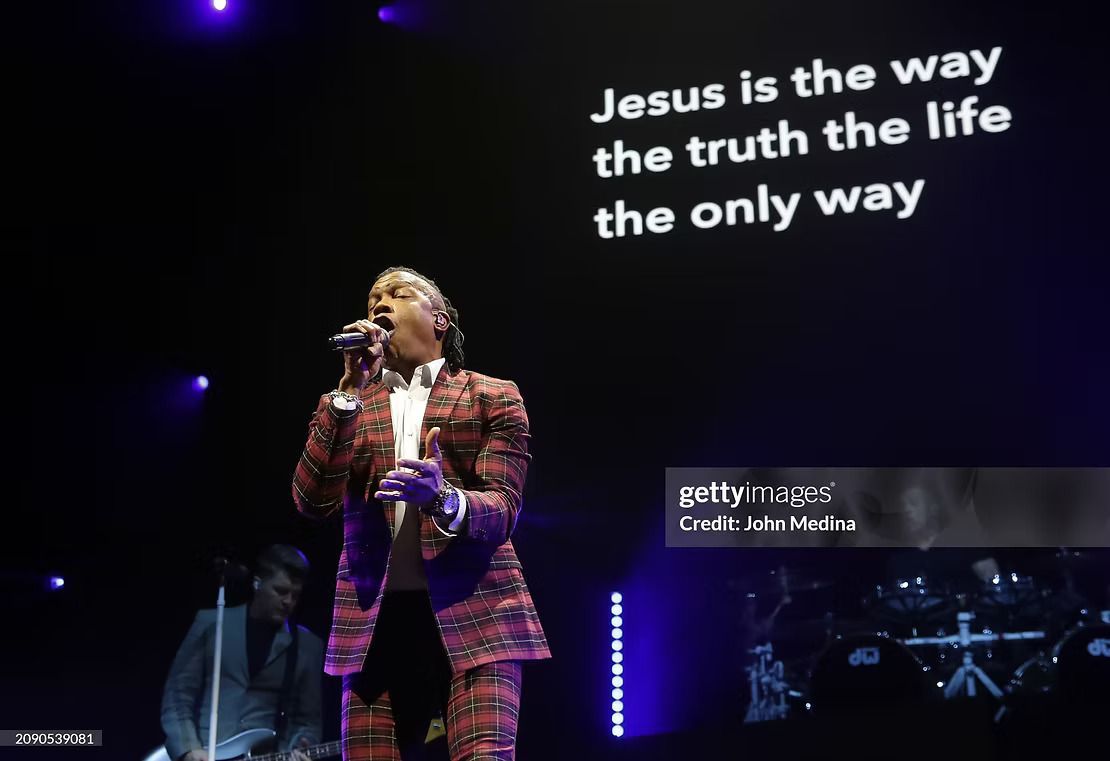 A singer in a patterned suit performs on stage, lyrics