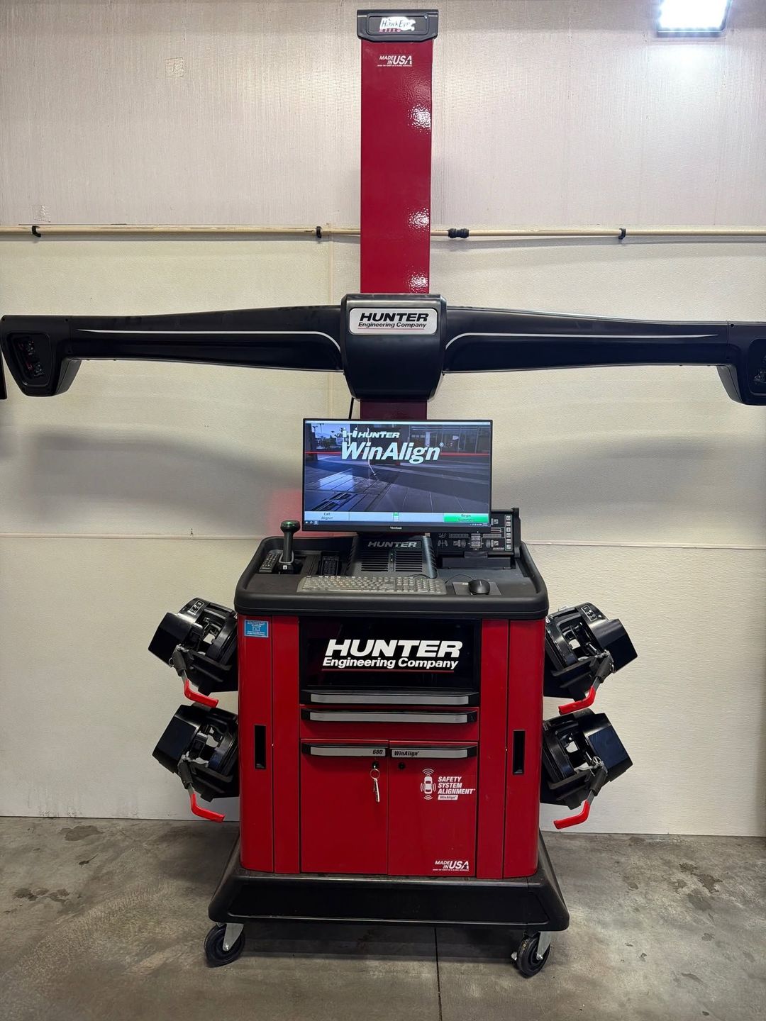 Red automotive alignment machine with monitor and adjustable arms in a workshop.