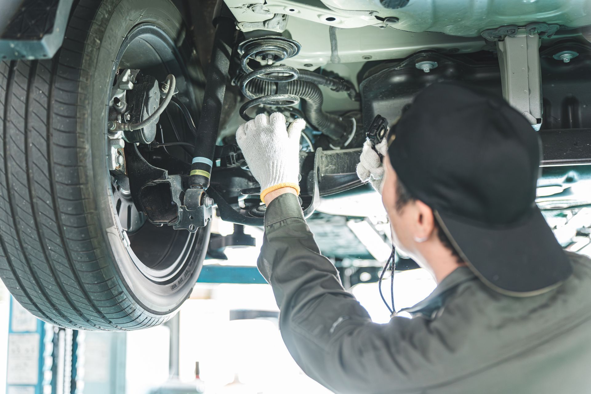 Mechanic inspecting a car’s suspension under a lifted vehicle in a garage