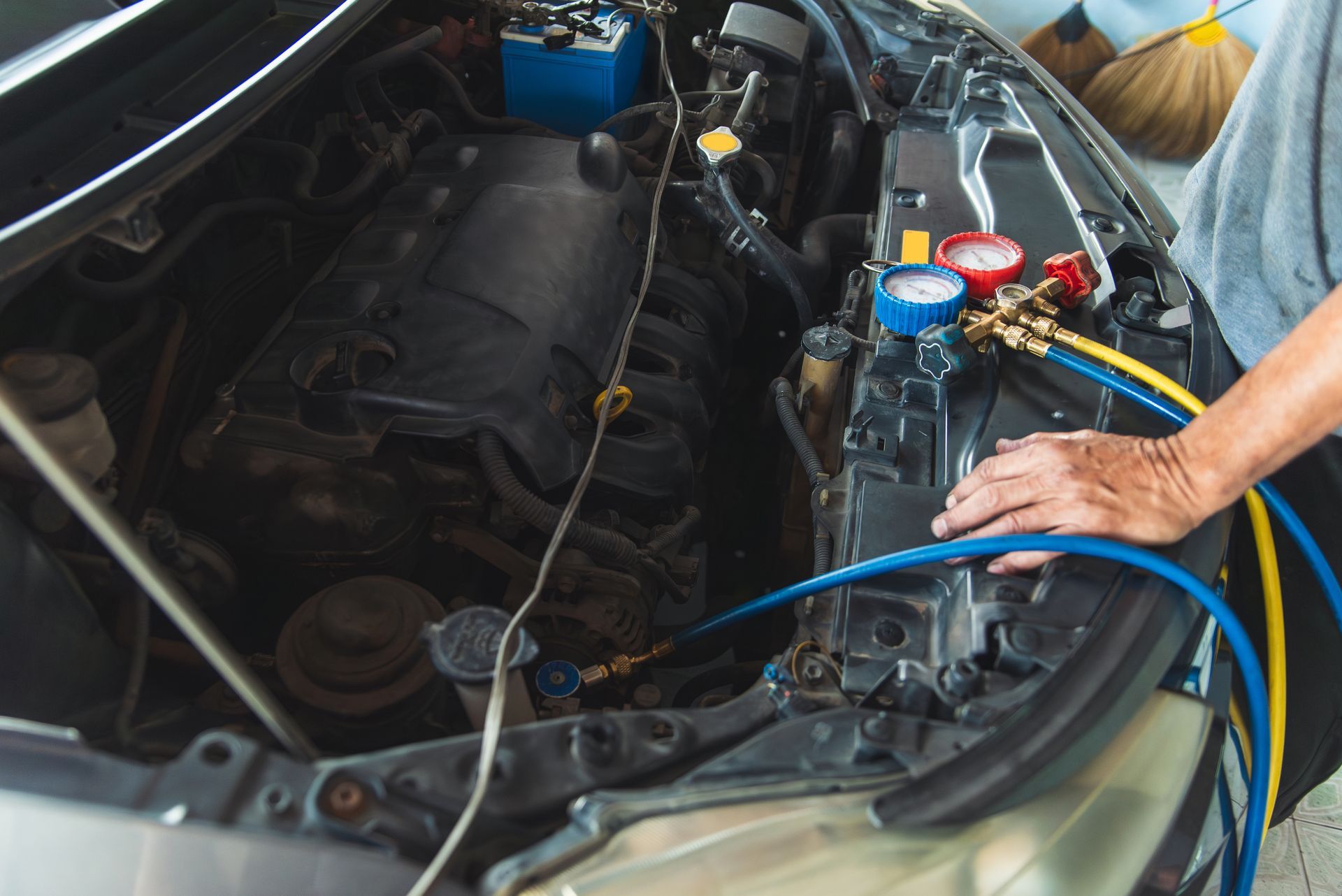 Person charging a car’s A/C system in an open engine bay with blue hoses and gauges
