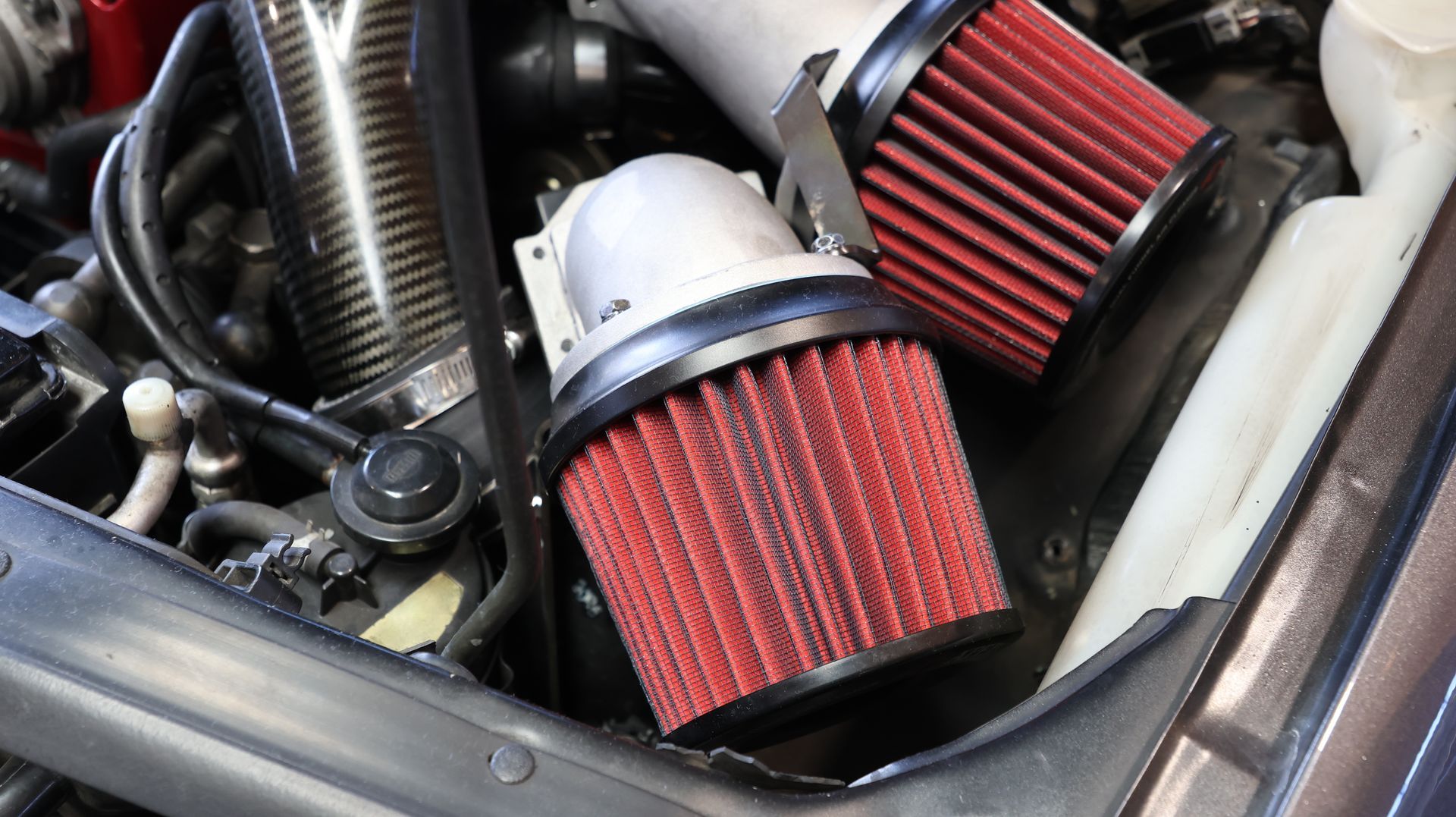 Two red cone air filters in a car engine bay, one with a silver cap.