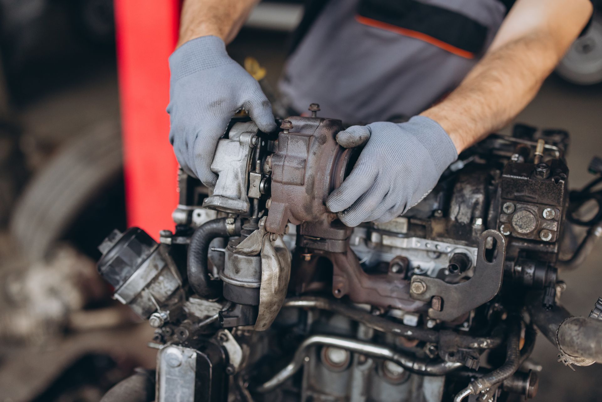 Mechanic wearing gray gloves repairs a rusty engine in a workshop