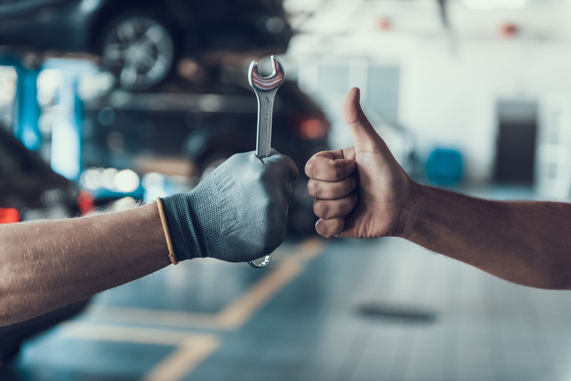 Two hands give a thumbs-up and a wrench bump in a workshop
