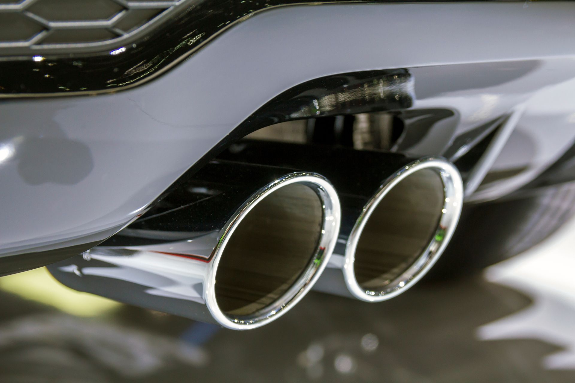 Close-up of a car’s chrome dual exhaust pipes beneath a gray rear bumper