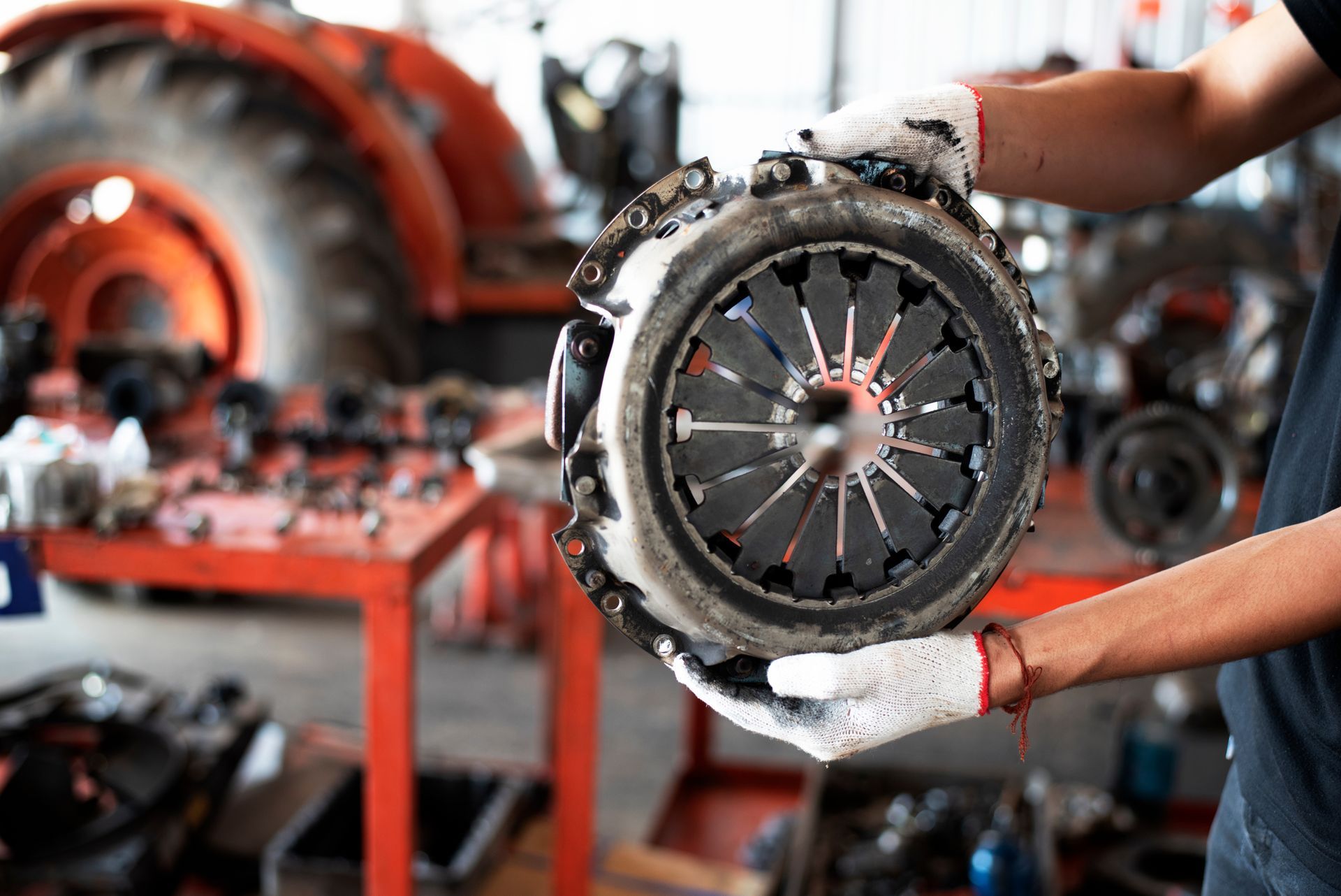 Mechanic holding a greasy clutch assembly in an auto repair shop with blurred tools in the background Mechanic holding a greasy clutch assembly in an auto repair shop with blurred tools in the background