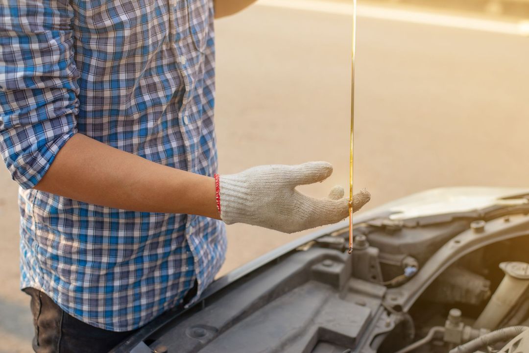 Person in a blue plaid shirt checking a car’s oil with a dipstick under the open hood