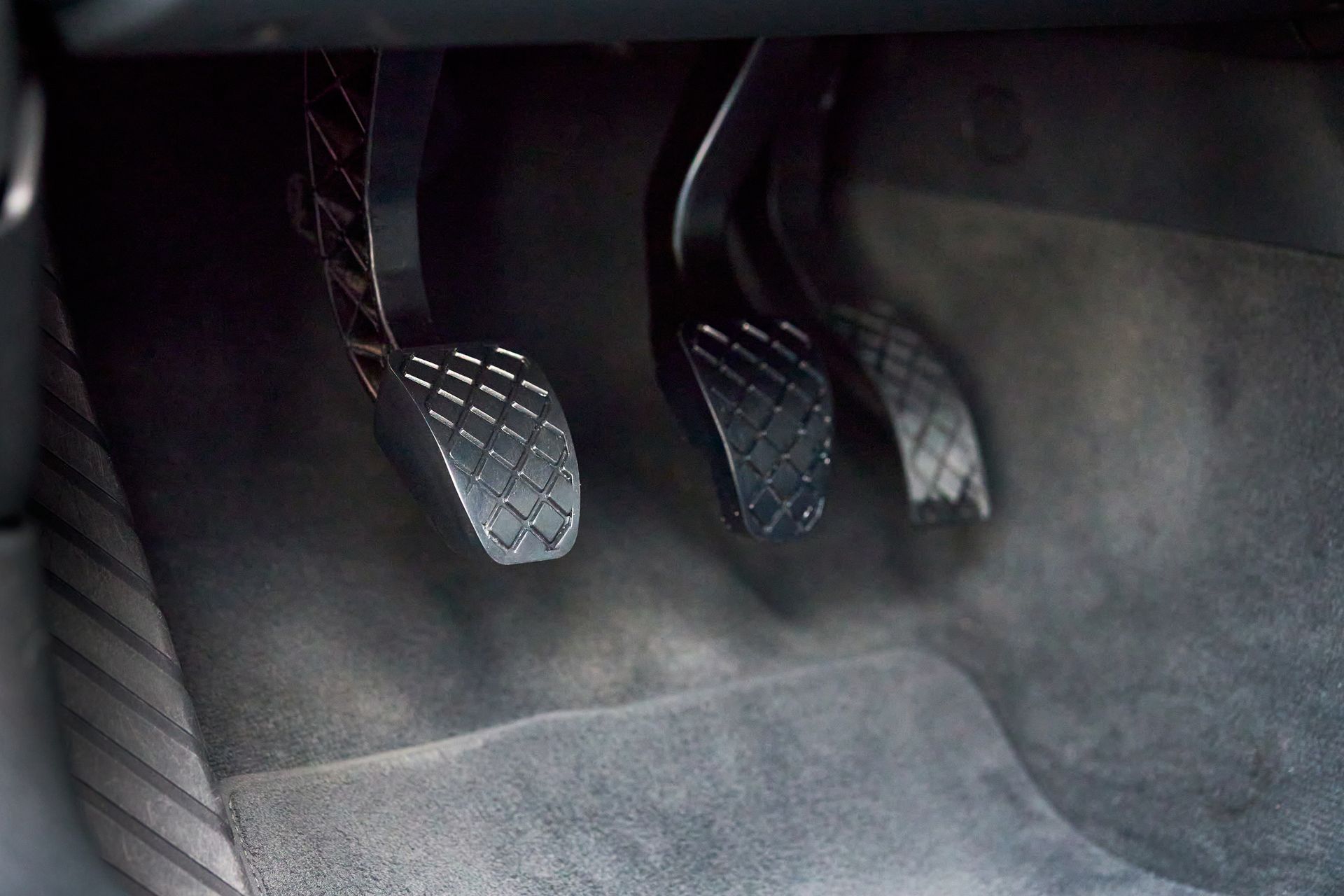 Car footwell showing three metal pedals with a textured accelerator, brake, and clutch on a dark floor mat Car footwell showing three metal pedals with a textured accelerator, brake, and clutch on a dark floor mat