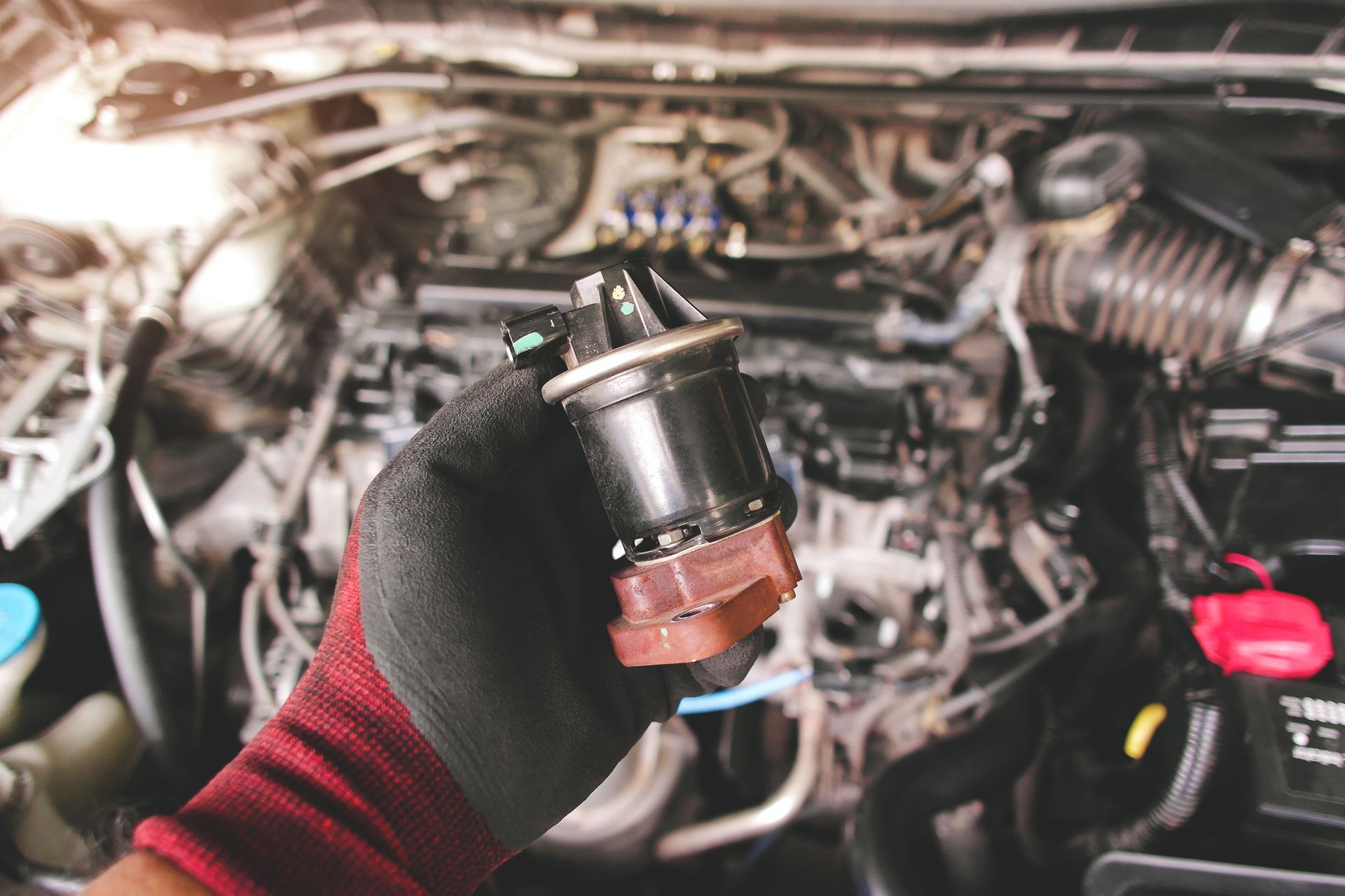 Gloved hand holding a small car engine part in an open engine bay