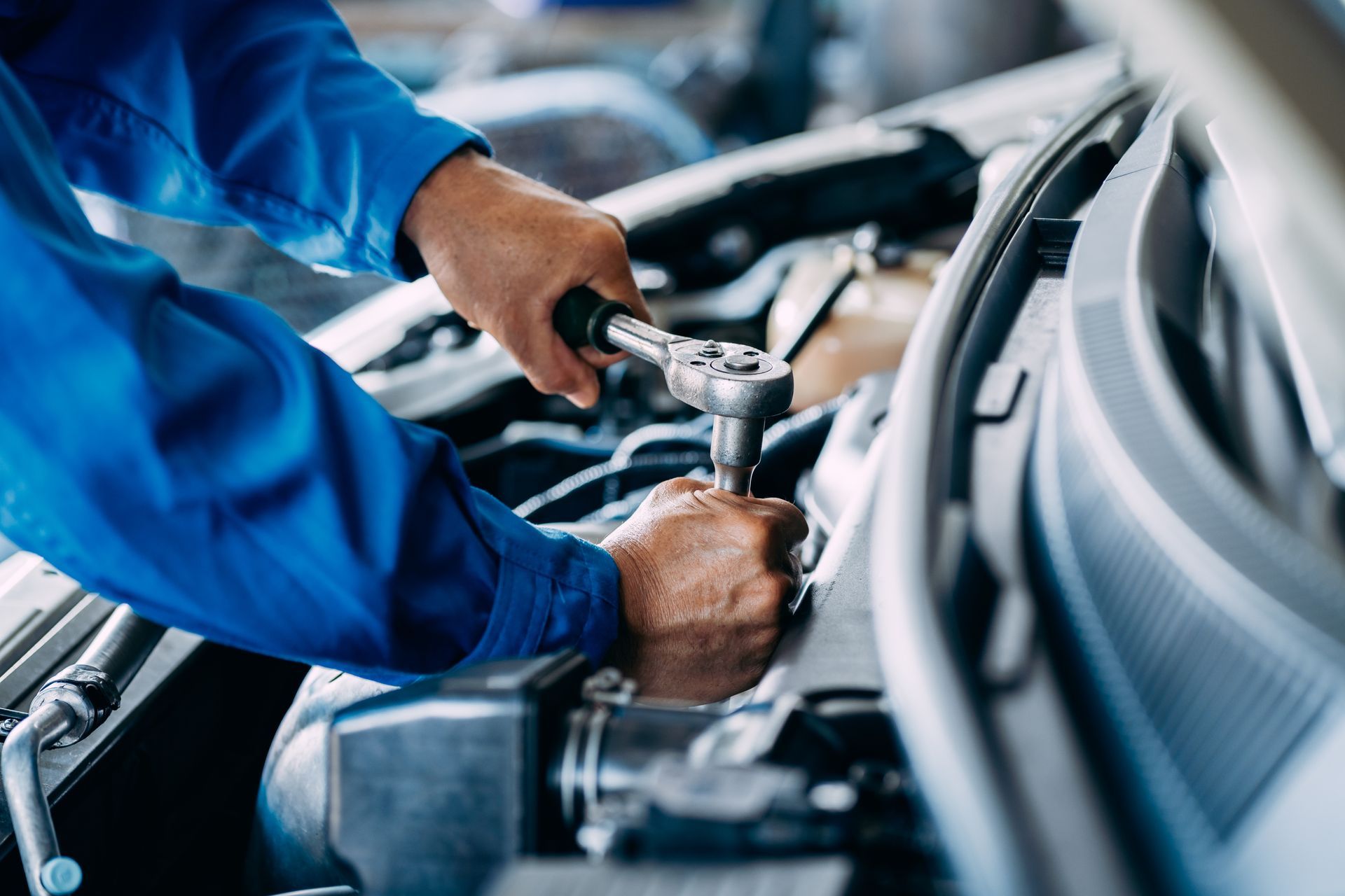 Mechanic in blue uniform tightening a car engine bolt with a wrench