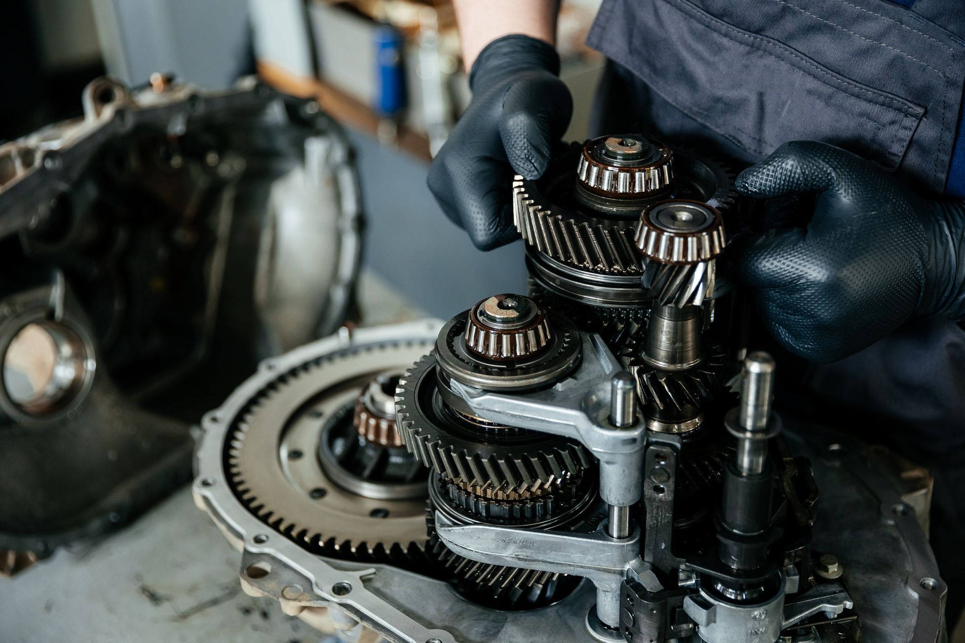 Mechanic’s gloved hands inspecting a metal gearbox with gears and bearings on a workbench Mechanic’s gloved hands inspecting a metal gearbox with gears and bearings on a workbench