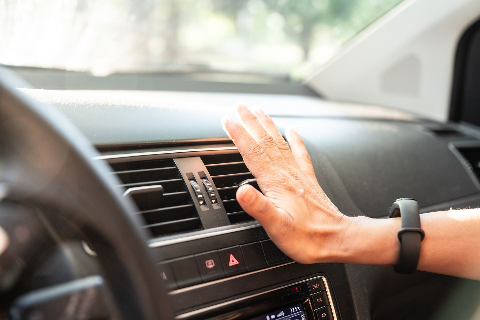 Hand using a car dashboard air vent, with a black smartwatch on the wrist.