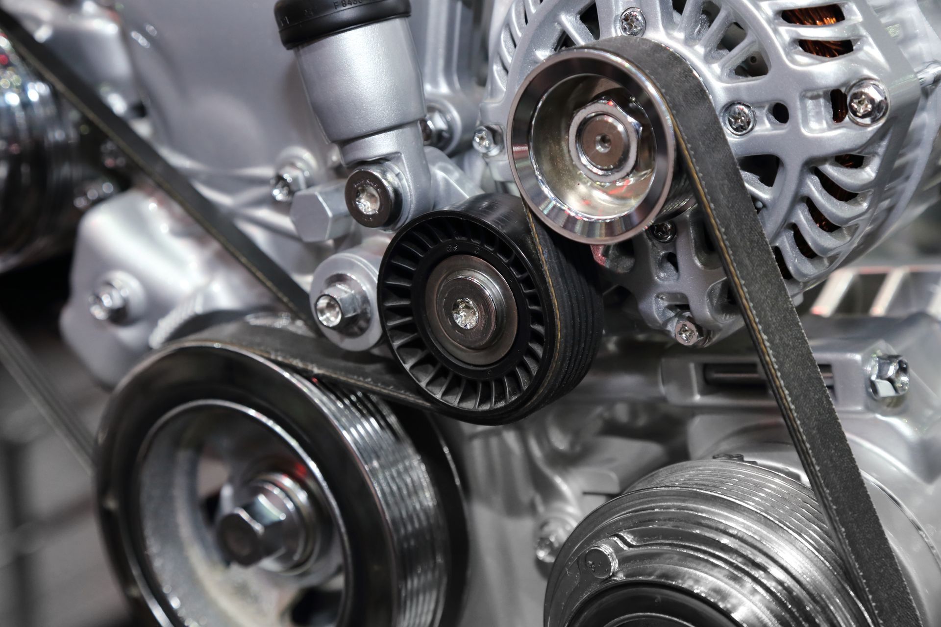 Close-up of a car engine’s belts, pulleys, and alternator in a metallic mechanical assembly Close-up of a car engine’s belts, pulleys, and alternator in a metallic mechanical assembly