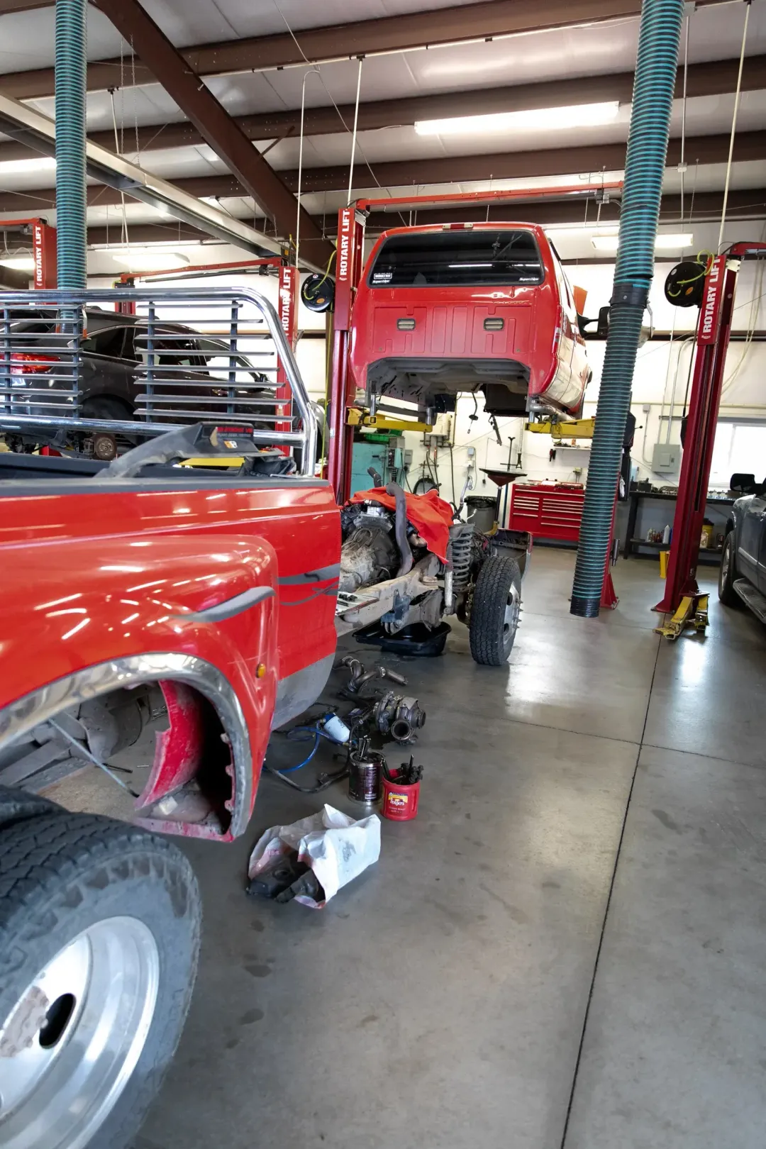 Red pickup truck in auto repair shop with mechanic working underneath and tools on the floor