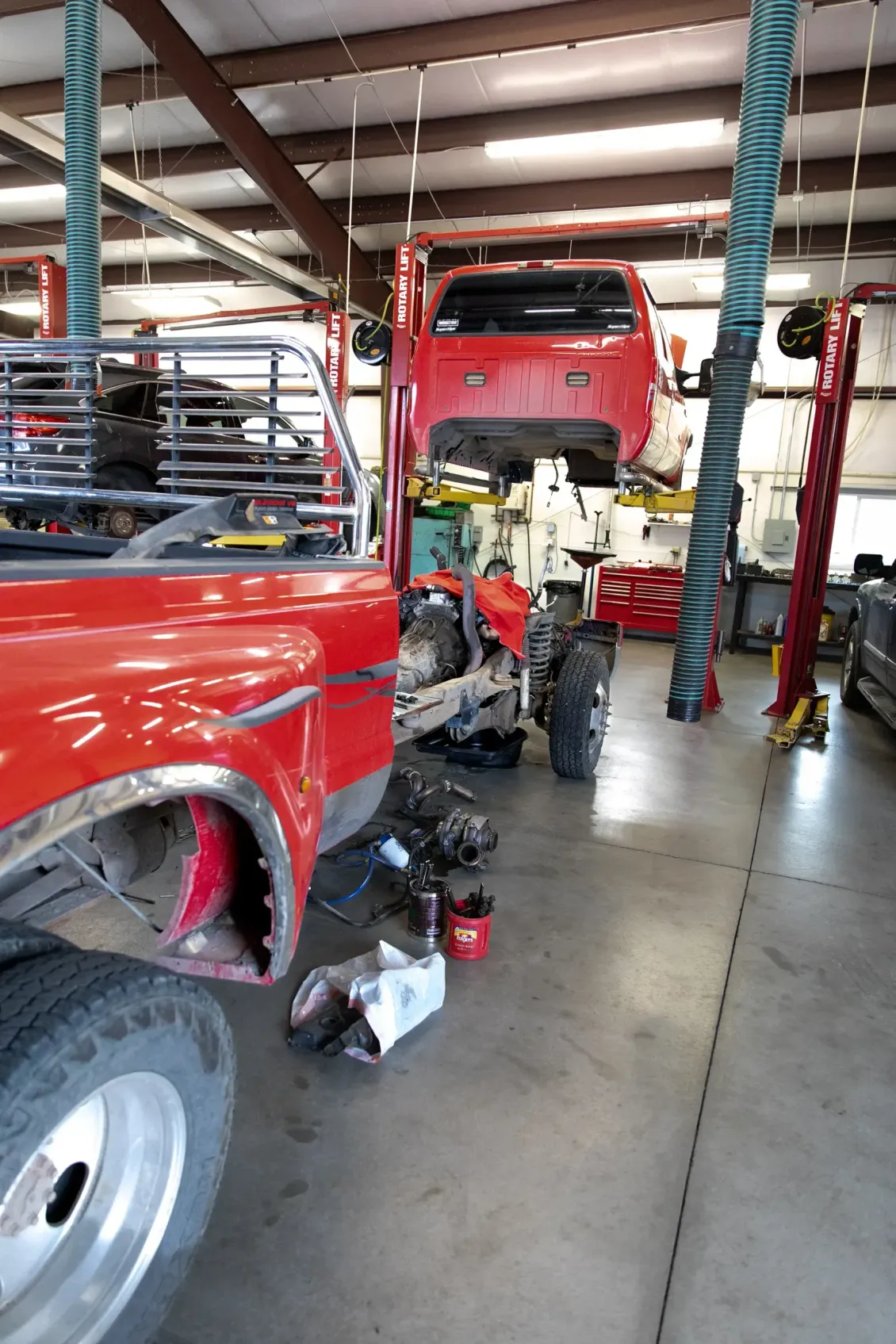 Red pickup truck in auto repair shop with mechanic working underneath and tools on the floor