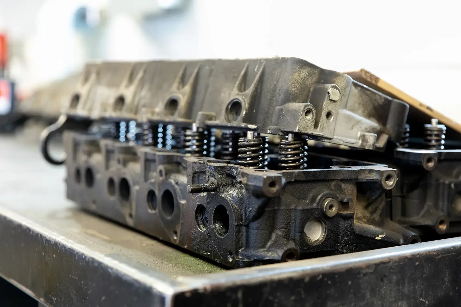 Metal engine cylinder head on a workbench, showing valve springs and machined ports.