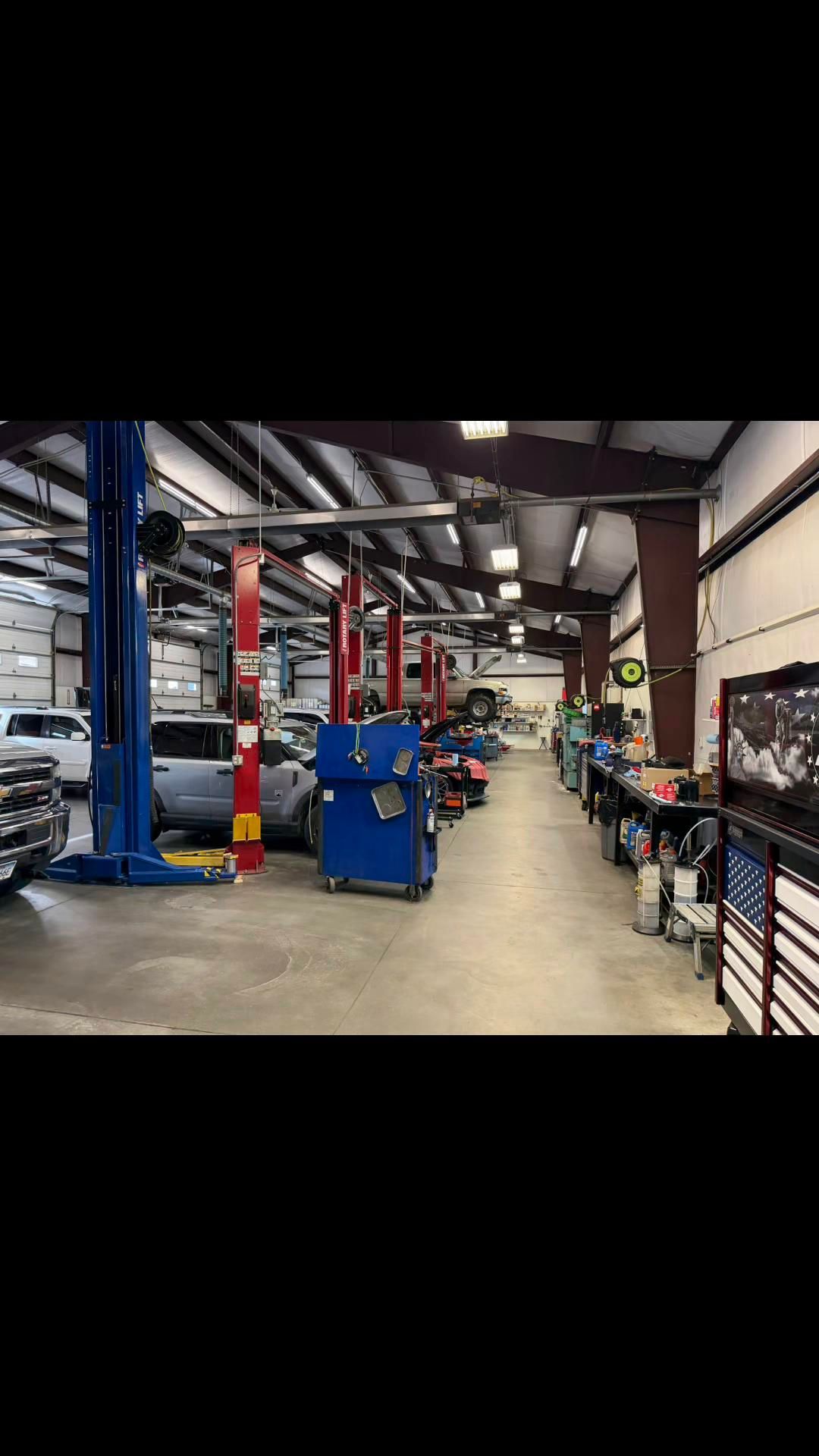 Mechanic working on a car on a lift in a modern auto repair shop, with a white SUV in the foreground