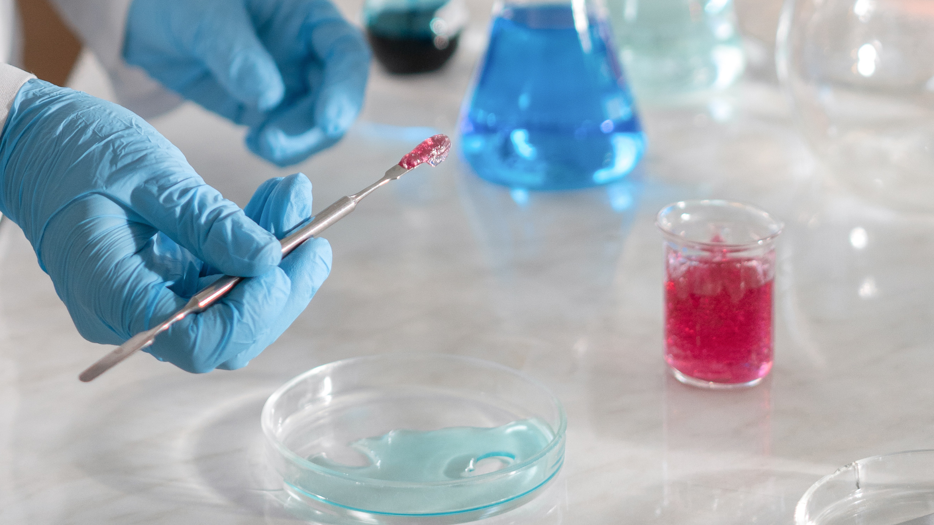 Gloved hand holding a swab over petri dishes and colored lab liquids in a laboratory setting