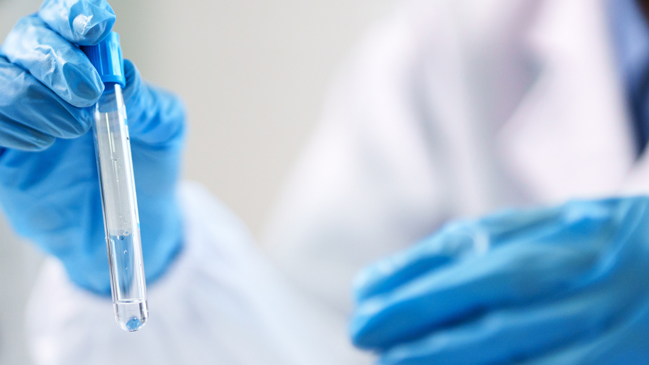 Blue-gloved hands holding a clear test tube in a lab setting