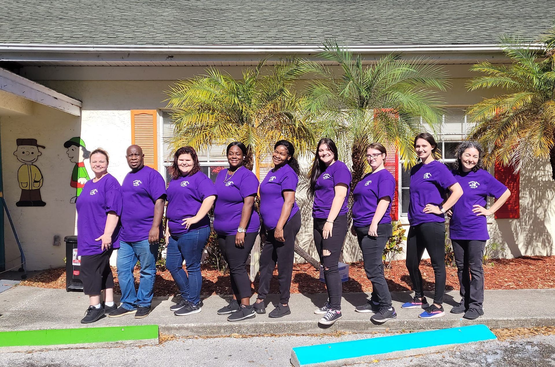 A group of people wearing purple shirts are standing in front of a building.