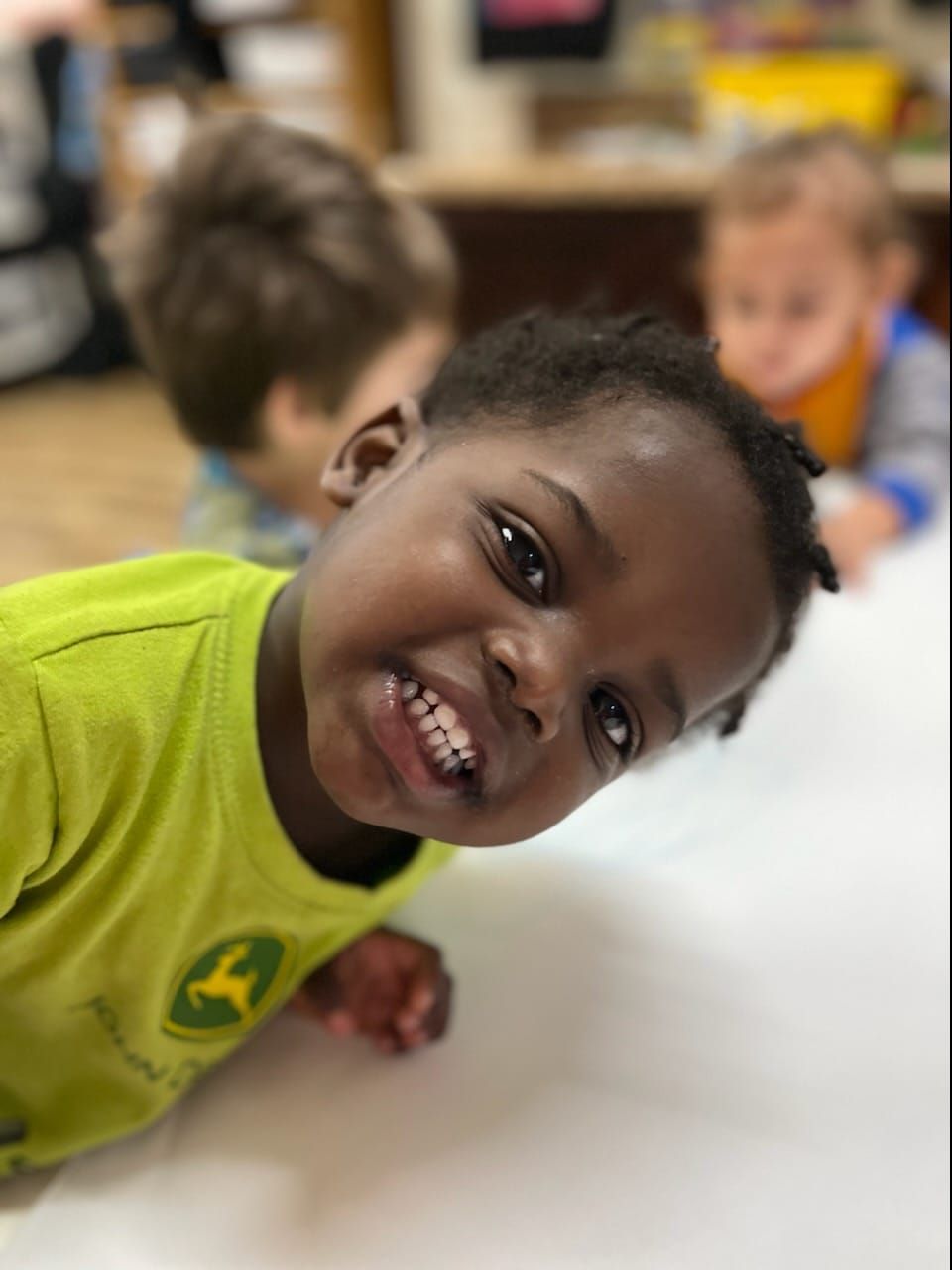 A young boy wearing a green john deere shirt smiles for the camera