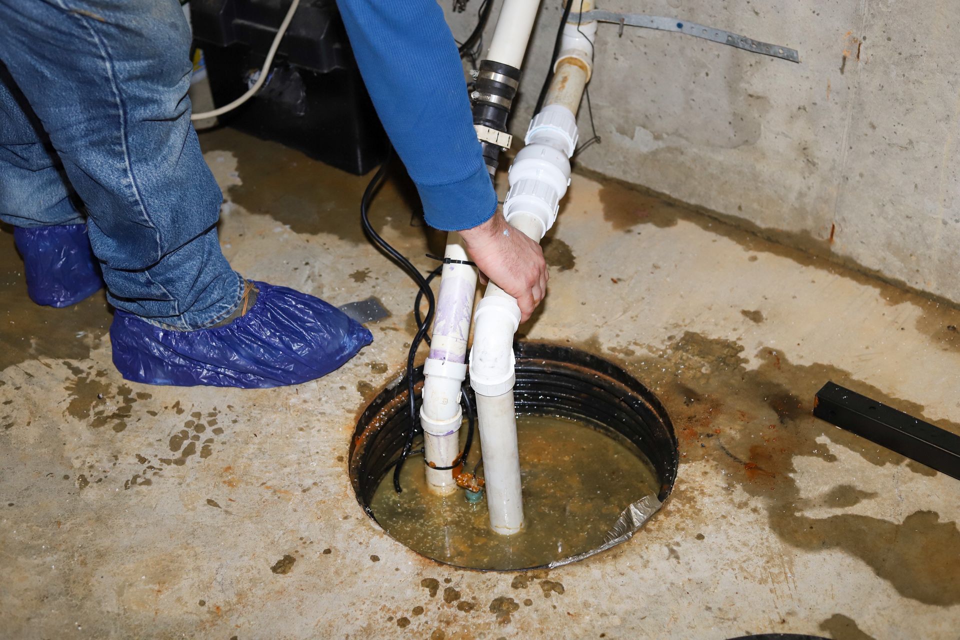 Worker using white pipes to access a sump pit in a concrete floor