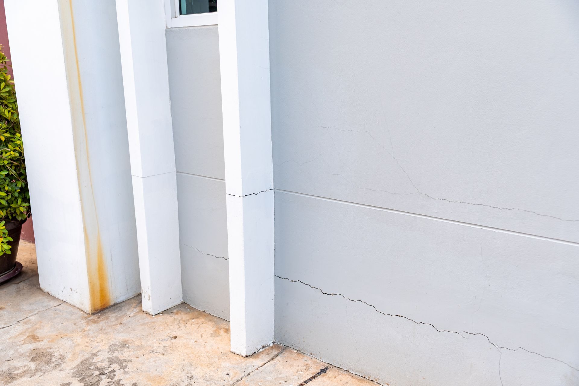 Cracked white exterior wall beside a doorway and concrete walkway