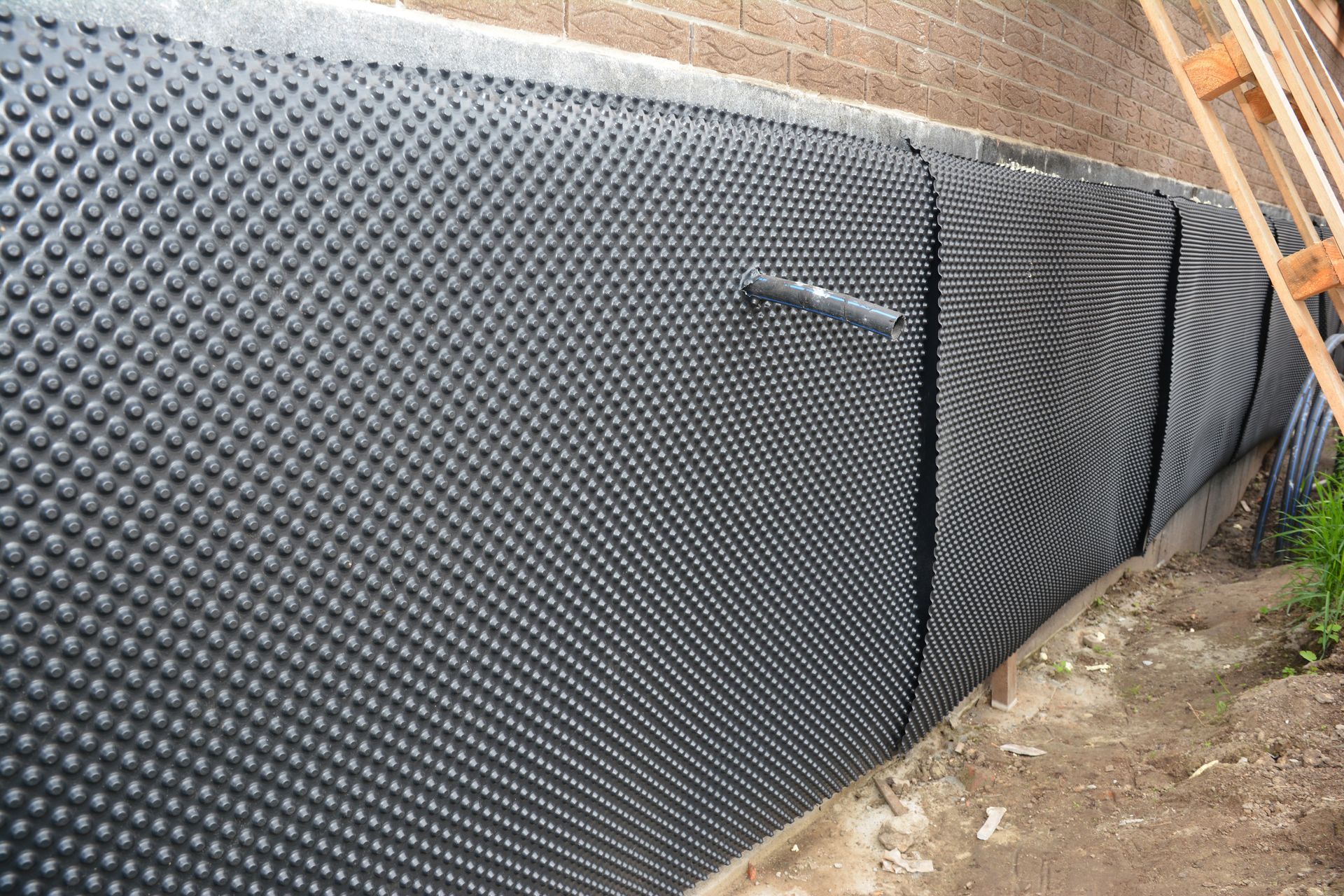 Black textured retaining wall panels along a dirt slope beside a fence and walkway.