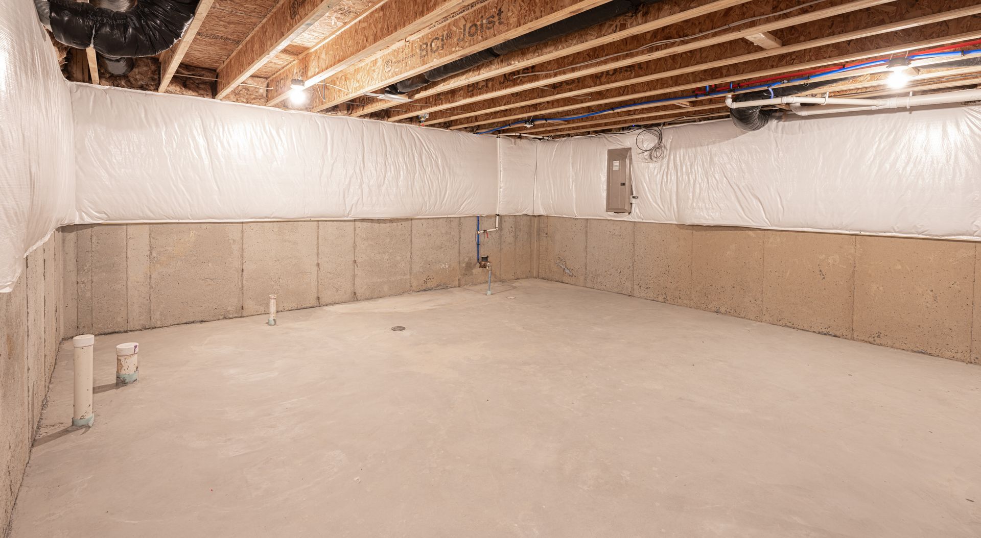 Empty unfinished basement with insulated walls, exposed ceiling joists, and concrete floor