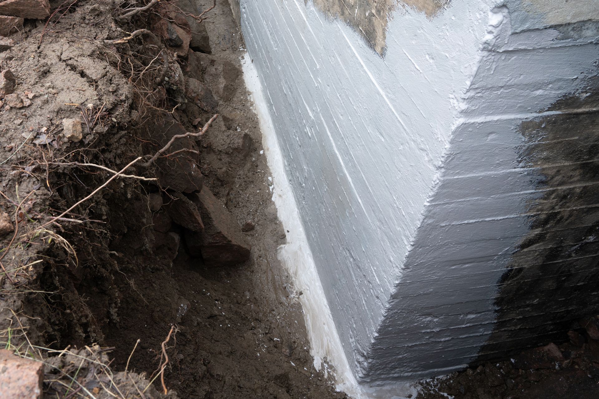 Excavated foundation corner with white insulation and exposed soil along a trench wall